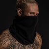 Up close of man with tattoos with a black polyester microfleece biogaiter over his face looking away from the camera