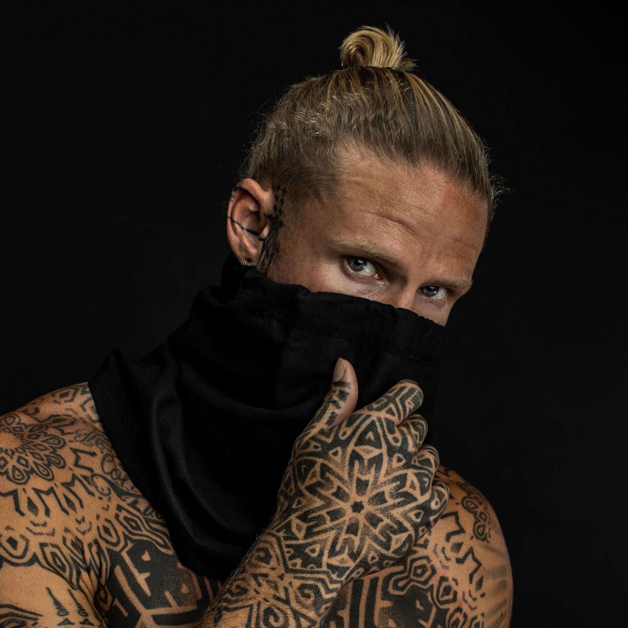 Young man with tattoos with black hemp and cotton biogaiter pulled up over his face 