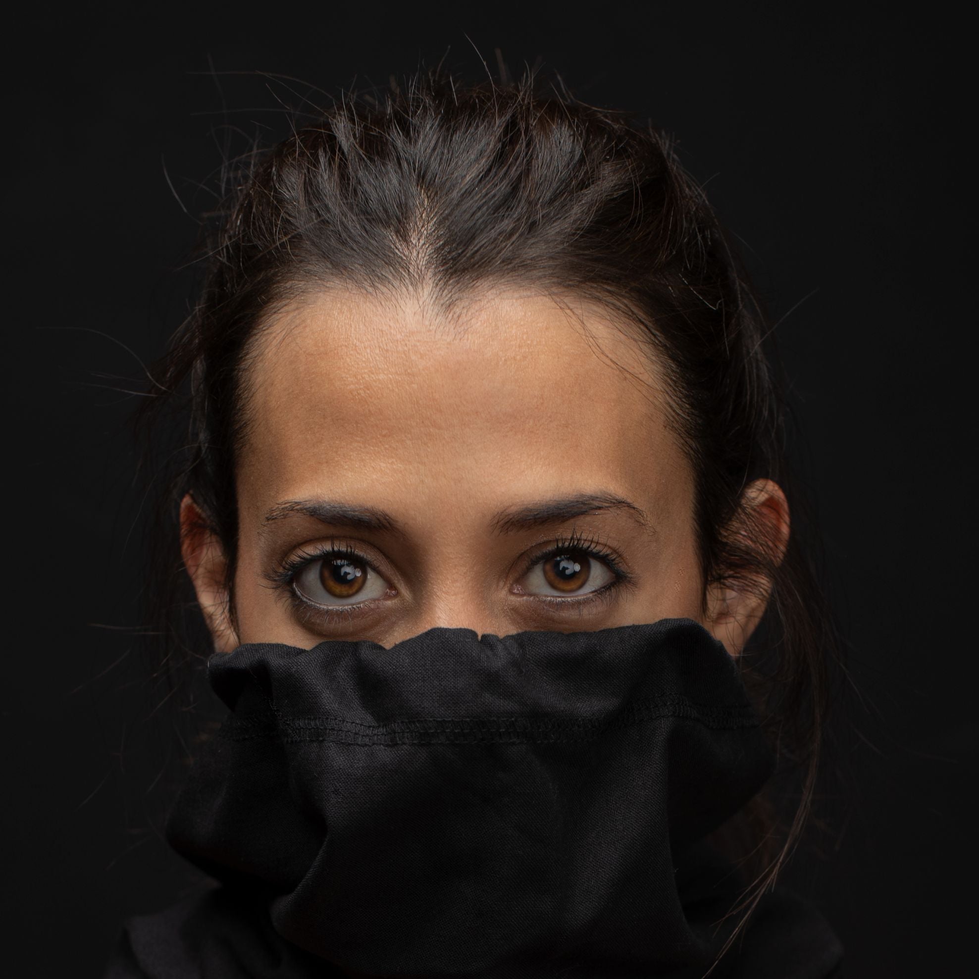 Young woman up close looking at the camera with a black hemp and cotton biogaiter pulled up over her face 