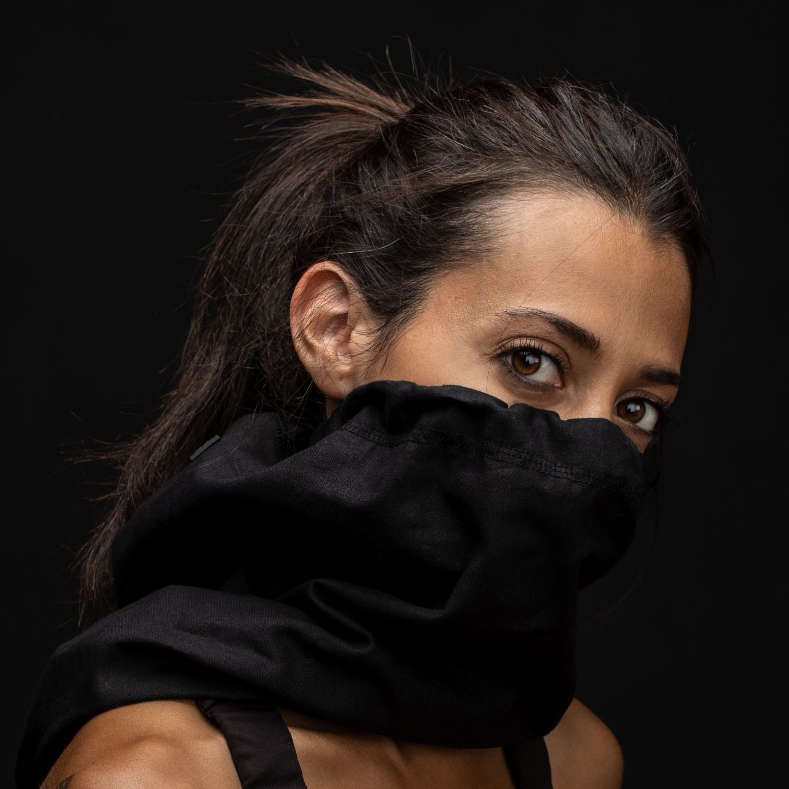 Young woman with pony tail looking at the camera with her head turned wearing a black hemp and cotton biogaiter pulled up over her face