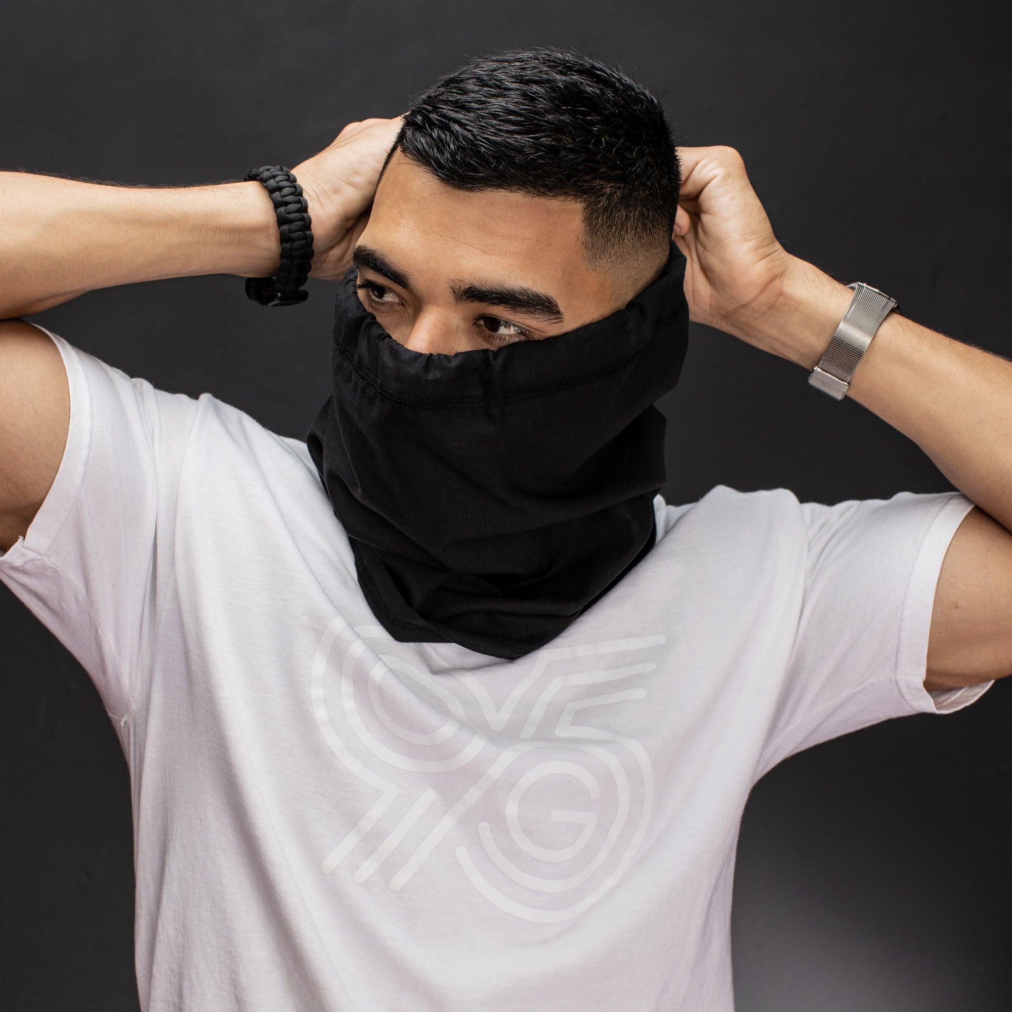 Young man with hands behind his head tightening a black hemp and cotton biogaiter that he has over his face wearing a white G95 Tshirt